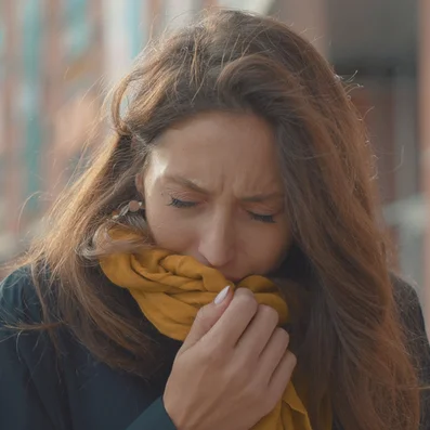 Frau mit akutem Hustenreiz hustet in ihren Schal.