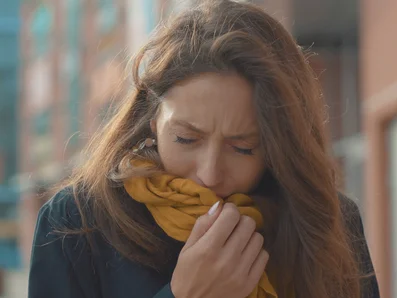 Coughs can be acute or chronic. Woman with acute coughing fits coughs into her scarf.