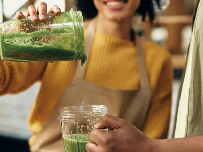 Frau schüttet gesunden Smoothie in ein Glas in der Hand eines Mannes.