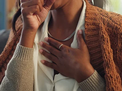 Coughing can be a symptom of a cold or acute bronchitis. Woman holds her hand to her chest and coughs into her other hand.