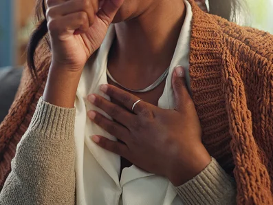 Frau hält die Hand an die Brust und hustet in die andere Hand.