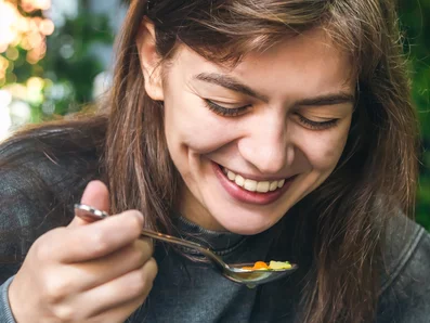 Frau isst Suppe und lacht dabei.