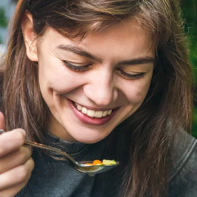 Frau isst Suppe und lacht dabei.