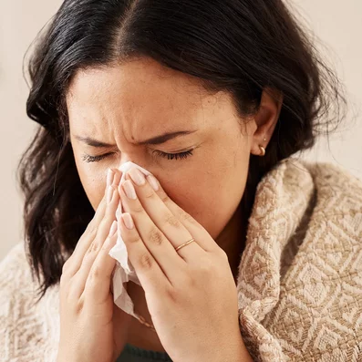 Frau schnäuzt sich die Nase.