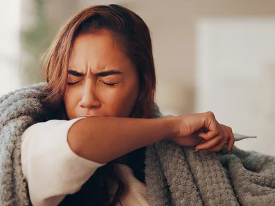 Woman with a cold coughs into the crook of her arm.