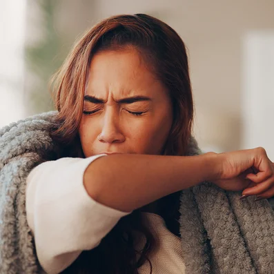 Frau mit Erkältung hustet in die Armbeuge.