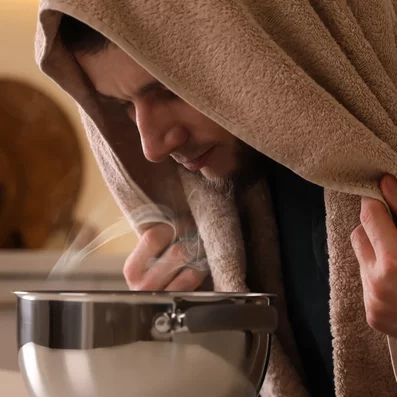 Mann mit Bronchitis inhaliert Kochsalzlösung am Küchentisch. 