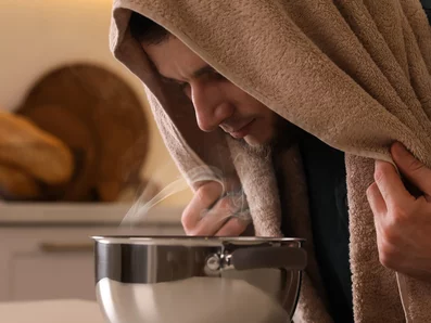 Mann mit Bronchitis inhaliert Kochsalzlösung am Küchentisch. 