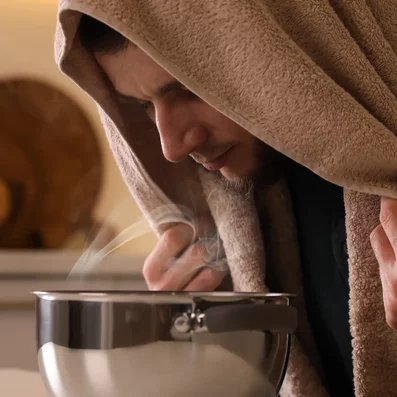 Mann mit Bronchitis inhaliert Kochsalzlösung am Küchentisch. 