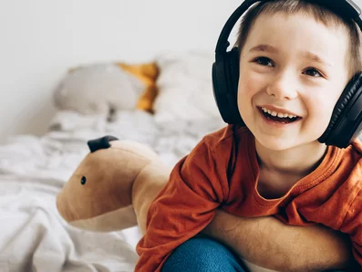 Kind sitzt auf einem Bett und hat Kopfhörer auf.