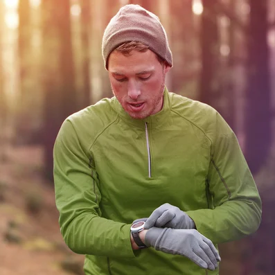 A man walks through a forest while looking at his watch.