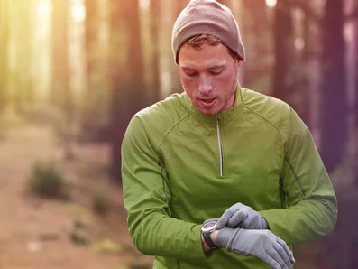 Mann läuft durch einen Wald und schaut dabei auf seine Uhr.