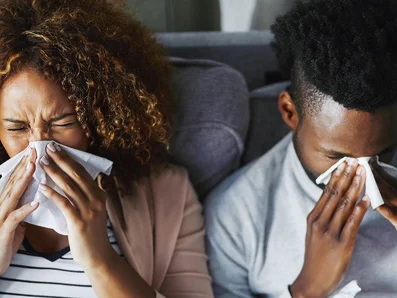 Frau und Mann mit Grippe oder Erkältung sitzen auf einer Couch.