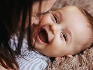 Mutter spielt mit lachendem Baby auf einem Teppich.