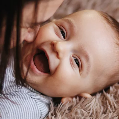 Mutter spielt mit lachendem Baby auf einem Teppich.